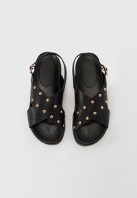 Svarta sandaler med korsade remmar, prydda med gyllene nitar, med en slingback-design och vadderad fotbädd. Slät yta.