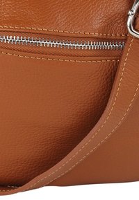 Bruine leren handtas met een gestructureerde afwerking. Voorzien van een zilverkleurige rits en contrasterende beige stiksels langs de randen.