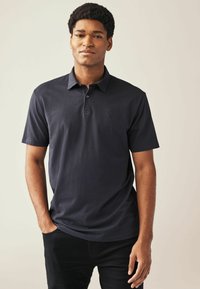 Polo náutico de algodón, con cuello, mangas cortas y un logo en el lado izquierdo del pecho. La tela parece suave y sin textura.