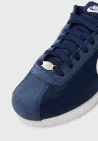 Sapatilha azul-marinho feita de camurça e tecido, com um upper texturizado, fecho de atacadores e um accentuador prateado do logótipo da Nike na língua.