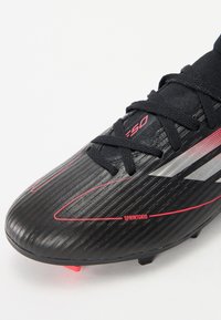 Black football boot with a textured surface, red accents, and gray stripes. Features a lace-up design and pointed studs for traction.