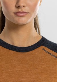 Short-sleeve shirt in burnt orange with a dark gray, ribbed collar. Features a logo stitched in dark thread near the shoulder seam.
