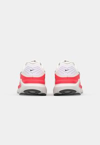 Chaussures de sport Nike avec une tige blanche et des accents roses, un talon texturé et une semelle grise, conçues pour le confort et le soutien.