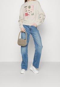 Felpa beige con logo "BOSS" multicolore, jeans larghi azzurro chiaro e borsa a tracolla beige con texture. Completa il look un paio di sneakers bianche.
