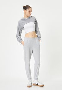 Grijze hoodie met een cropped ontwerp en lange mouwen, gecombineerd met bijpassende grijze joggers met een elastische tailleband en cuffs. Witte sneakers maken de look compleet.