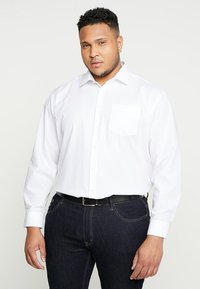 Witte lange mouw dress shirt met een voorzak, knoopsluiting en een standaardkraag. Gecombineerd met donkere spijkerbroeken en een zwarte riem.