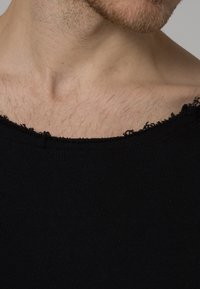 Débardeur noir à côtes avec un large décolleté, présentant des bords effilochés et une coupe ajustée. La texture semble douce et élastique.