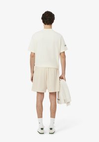 Un haut crème à manches courtes et un short assorti avec un design texturé. Tenant une légère veste, associé à des chaussettes blanches et des chaussures avec des accents verts.