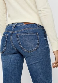 Mörkblå denim jeans med slim fit, med två bakfickor och en brun läderetikett ovanför midjan. Visibla blekta områden.