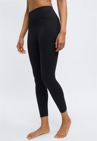 Schwarze Leggings mit hohem, geripptem Bund. Enganliegendes Design mit glatter Textur und Nahtdetails. Keine sichtbaren Muster oder Akzente.