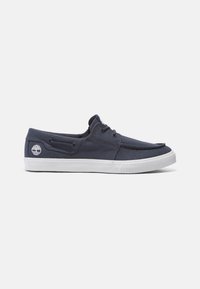 Marineblaue Canvas-Schlüpfschuhe mit einer weißen Gummisohle, seitlichem Schnürverschluss, runder Zehenform und einem Logopatch an der Ferse.