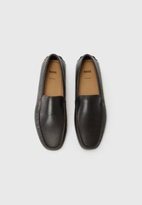 Mocasini din piele neagră cu un finisaj texturat, vârf rotund și interior maro, cu cusături subtile de-a lungul marginii și accesorii tonale.
