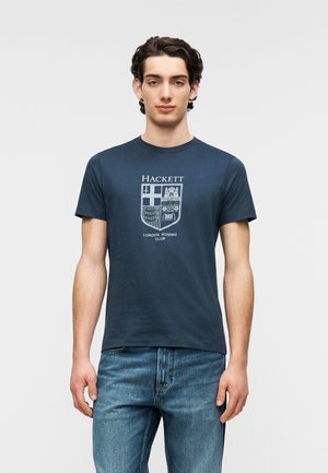 Tricou din bumbac albastru marin, cu un grafic alb reprezentând un scut pe centru, cu textul „Hackett” și „London Rowing Club”. Mâneci scurte.