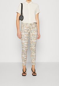 Krémová košile s krátkým rukávem, vzorované slim-fit kalhoty v pastelových barvách s paisley designem a černé sandály na popruhy. Doplňujícím prvkem je malá černá taška.