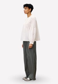 Blouse blanche, ample, avec des manches ballons et des détails de coutures verticales, associée à un pantalon large rayé noir et blanc et des chaussures métalliques.
