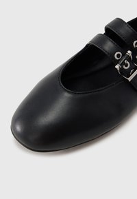 Chaussure en cuir noir présentant un bout arrondi, un design à double bride avec des boucles argentées, et une texture lisse.