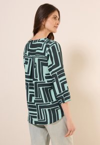 Langarmtop met een geometrisch zwart en mint patroon. Gemaakt van een lichte stof met een losse pasvorm en een ronde hals.