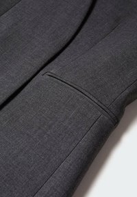Tela de chaqueta de traje gris con una textura suave, que muestra un detalle de bolsillo ajustado en la manga y elementos de diseño minimalistas.