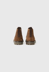 Botines de ante marrón con una textura suave, paneles laterales elásticos y una suela de goma duradera con un patrón de dibujo.