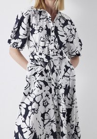 Kortärmad klänning med blommönster i svart på vit bakgrund, med krage, knappar framtill och bälte i midjan.