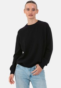 Pull noir à col rond avec manches longues et coupe décontractée, fabriqué dans un tissu doux et texturé, assorti à un jean bleu clair.