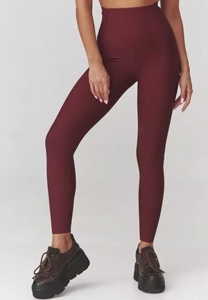 Burgundowe legginsy o wysokim stanie z prążkowaną teksturą, dopasowanym fasonie i elastycznym materiale. Połączone z czarnymi trampkami na platformie.