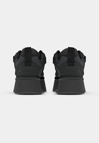 Sorte treningssko med et kraftig design, teksturert overdel og solid hæl. Har en bakre trekkstropp og minimal merkevare.