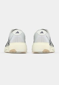 Γκρι και λευκά αθλητικά παπούτσια με ανώτερο μέρος από πλέγμα, λαστιχέ�νια σόλα και τρεις πιο σκούρες ρίγες· στρογγυλεμένο τακούνι και λογότυπο στο πίσω μέρος.