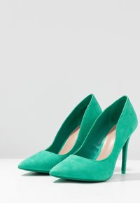 Escarpins en daim vert à talon haut avec un bout pointu et une doublure intérieure lisse. Les chaussures présentent un design élégant avec un talon aiguille haut.