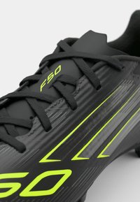 Black soccer cleat with textured synthetic upper, featuring bright green "F50" logo and lateral stripes. Laced design with durable accent.