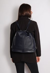 Zaino in pelle blu navy fatto a mano, con una texture morbida, chiusura con cordoncino e due tasche con zip sulla parte anteriore. Spallacci regolabili.