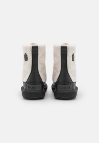 Botas de tobillo de piel sintética blancas y negras se exhiben, con un logo negro y material texturizado, sobre un fondo blanco liso.