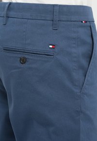 Blue textured shorts featuring a single back pocket with a black button and a small logo patch in red, white, and blue.