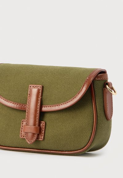 Μικρή υφασμάτινη ώμου τσάντα σε ελιά πράσινο με καφέ δερμάτινο διάκοσμο, λεπτομέρεια με πόρπη και χρυσό μεταλλικό δαχτυλίδι στο πλάι σε λευκό φόντο.