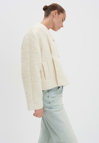 Ivory gekleurde textuurjacket met een cropped snit, featuring een dubbele knoopsluiting en zijzakken, gecombineerd met lichtblauwe spijkerbroek.