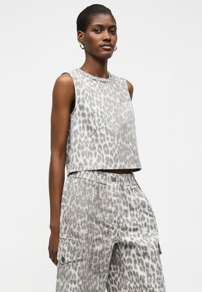 Γυναίκα φορώντας αμάνικη κοντή μπλούζα με λεοπάρ μοτίβο και ταιριαστό ψηλόμεσο παντελόνι cargo, στέκεται μπροστά σε απλό, φωτεινό φόντο.