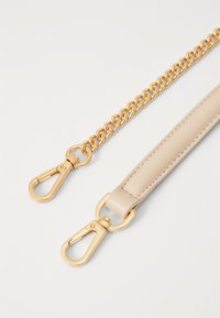 Brassard en cuir beige avec une chaîne dorée, comportant des fermoirs en forme de pince de homard et une texture lisse. Les maillons de la chaîne sont ronds et espacés de manière uniforme.