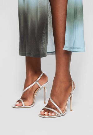 Silver high-heeled sandals with sparkling straps, open-toe design, and stiletto heels. Glossy finish and minimalist aesthetic.