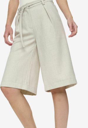 Beige weite Shorts in Knielänge mit Gürtelschlaufen und einem Stoffgürtel, getragen von einer Person mit sichtbaren Händen und unteren Beinen.