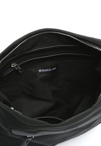 Unutrašnjost crne kožne torbe s glatkom teksturom, džepom sa patentnim zatvaračem i oznakom "MISAKO". Zatvaranje s patentnim zatvaračem na vrhu.