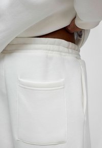 Witte sweatpants hebben een gladde, zachte textuur met een elastische tailleband en een enkele patchzak aan de rechterkant.