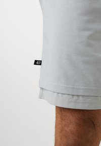 Light blue cotton shorts featuring a rolled hem, panel design, and a black brand tag on the side. Smooth texture and casual fit.