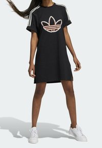 Abito t-shirt in cotone nero con maniche arrotolate, spacchi laterali e logo Adidas multicolore sul petto. Presenta strisce bianche sulle spalle.