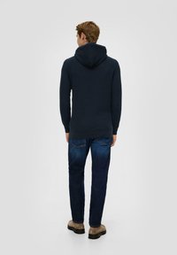 Marineblauer Kapuzenpullover mit langen Ärmeln, geripptem Muster und lockerer Passform, kombiniert mit dunkelblauen Jeans und beigen Knöchelstiefeln.