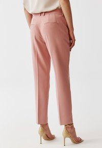 Světlé růžové kalhoty na míru se slim fit střihem, obsahující dvě zadní kapsy a plochý pás. Nosené s béžovými lodičkami na vysokém podpatku.