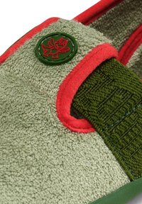 Zielony tekstylny but z chropowatym wierzchem, czerwonymi akcentami i zielonym okrągłym logo z postacią z kreskówki. Płaska gumowa podeszwa.