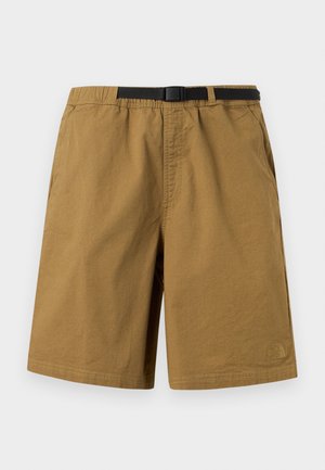 Ruskeat rennot shortsit, joissa musta säädettävä solkivyö, sivutaskut ja hillitty logo alavasemman jalan kohdalla yksiväristä taustaa vasten.