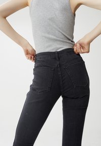 Los jeans de mezclilla gris oscuro presentan un diseño ajustado con bolsillos traseros y una cintura alta. La costura visible añade textura al material.