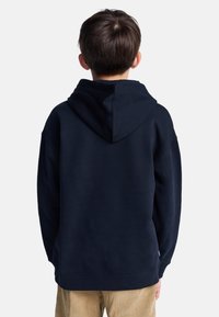 Felpa blu navy con cappuccio regolabile, maniche lunghe e polsini a coste. Tessuto morbido e vestibilità rilassata, indossata con pantaloni di velluto a coste beige.