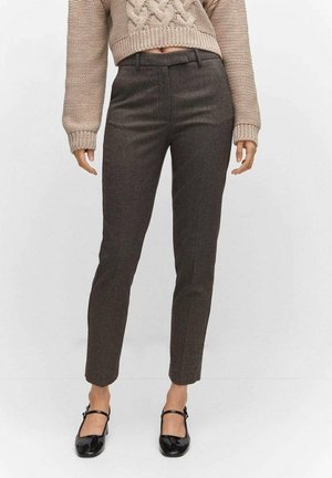 Brown houndstooth trousers with a slim fit and cropped length, paired with a beige cable-knit sweater and black patent Mary Jane shoes.
